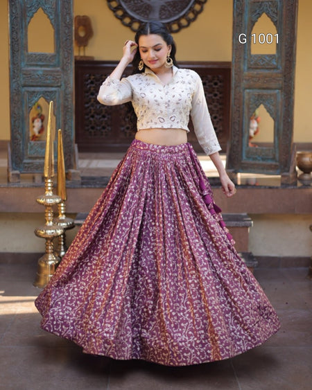 A woman modeling a traditional Indian outfit featuring a white embroidered crop top and a voluminous purple skirt with a white floral pattern, set against an ornate courtyard background.