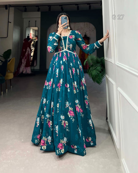 Person wearing a teal floral dress in a room with white walls and a plant.