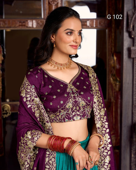 Woman wearing a traditional purple and green saree with gold embroidery, posing indoors.