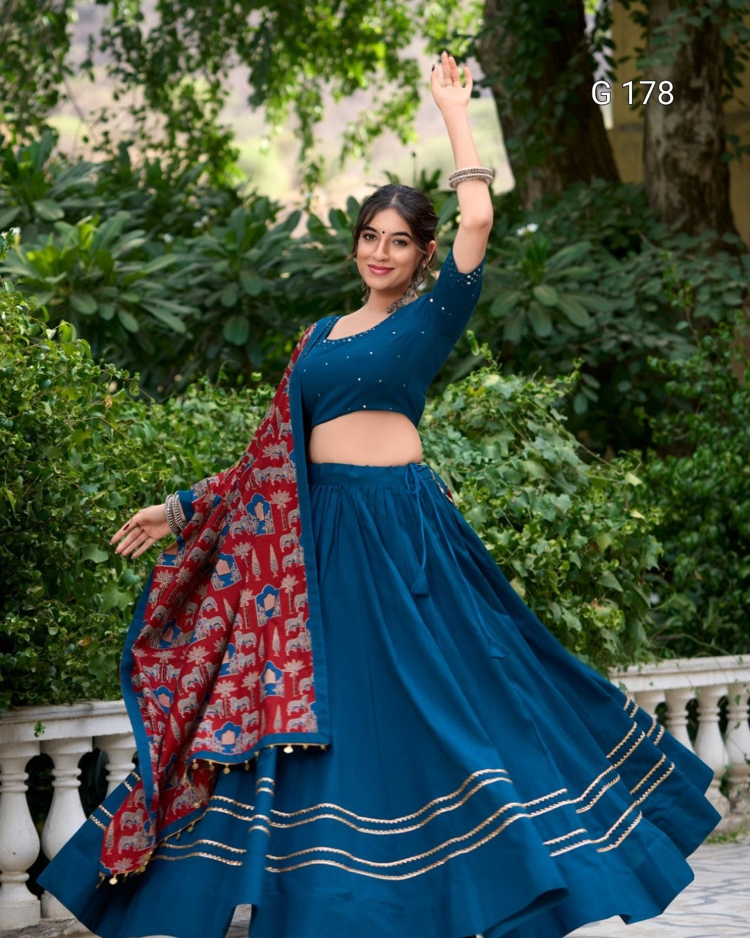 Woman in a blue traditional outfit with a red and gold dupatta, standing outdoors.