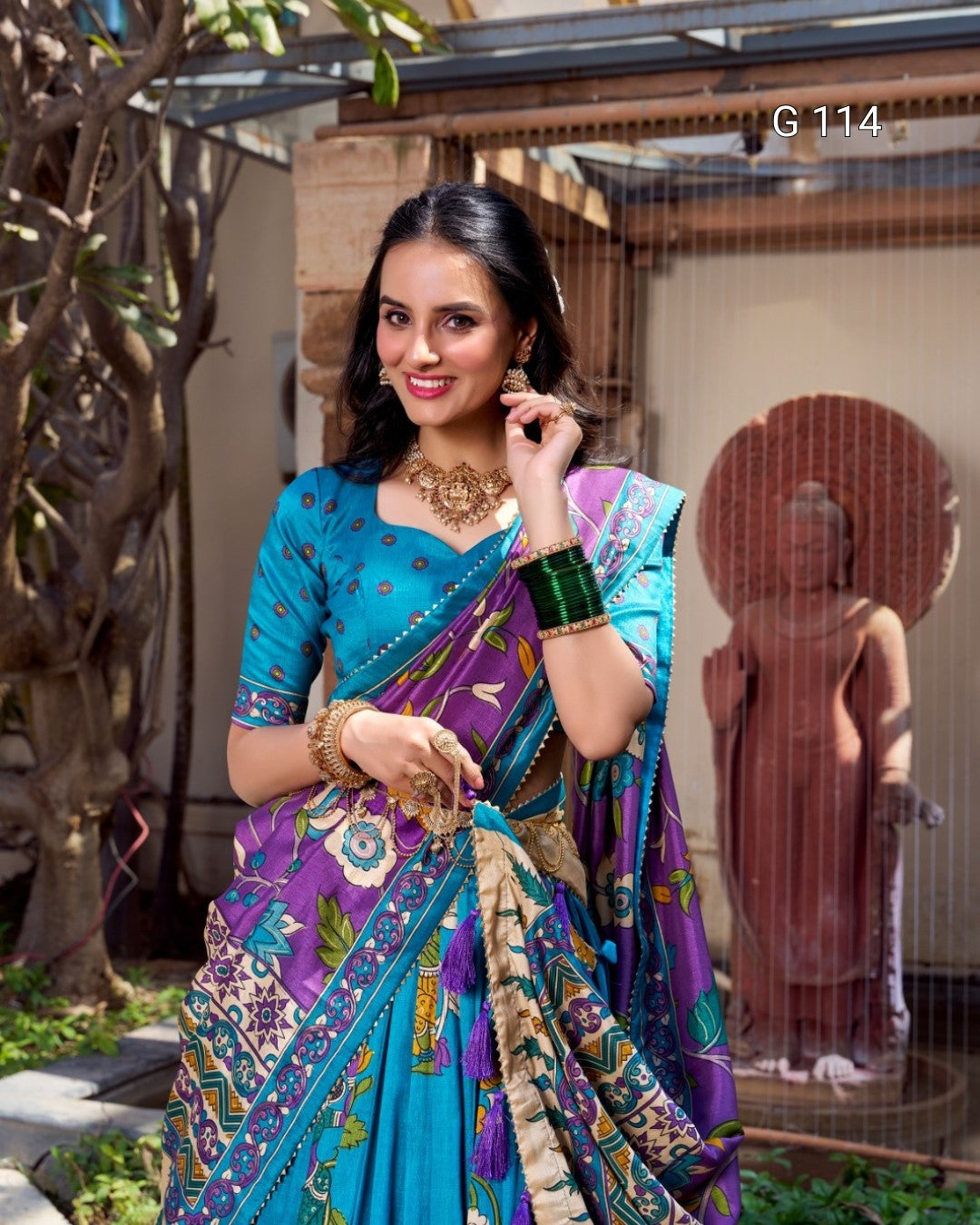 Woman in a colorful saree standing outdoors with a statue in the background