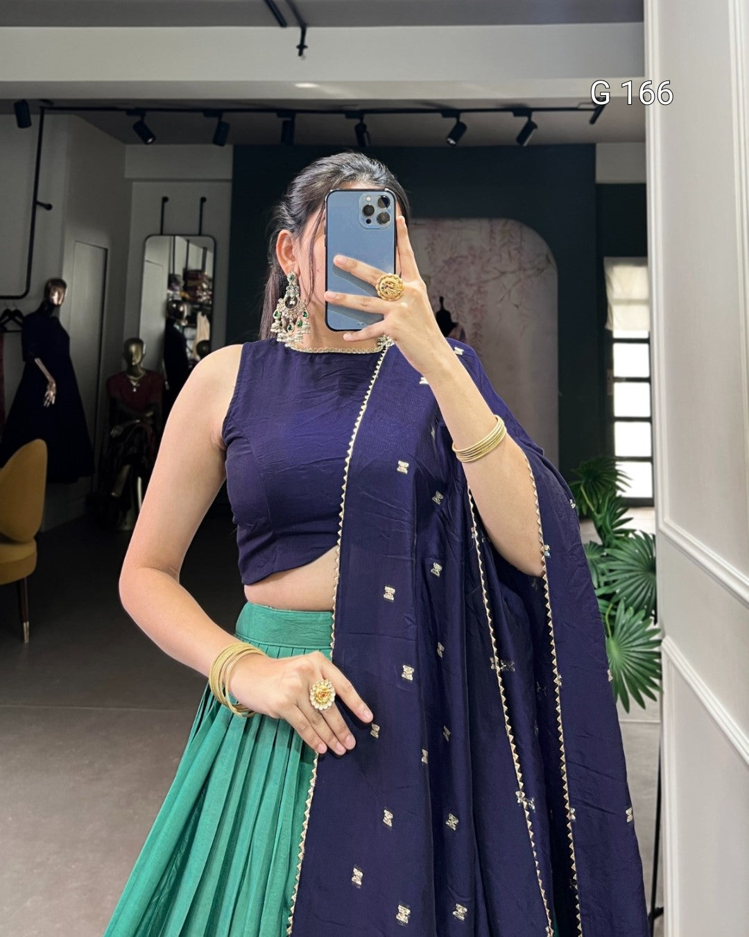Person wearing a blue top and green skirt with a matching dupatta in a room.