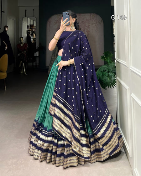 Woman wearing a traditional outfit with a blue and green saree in a room.