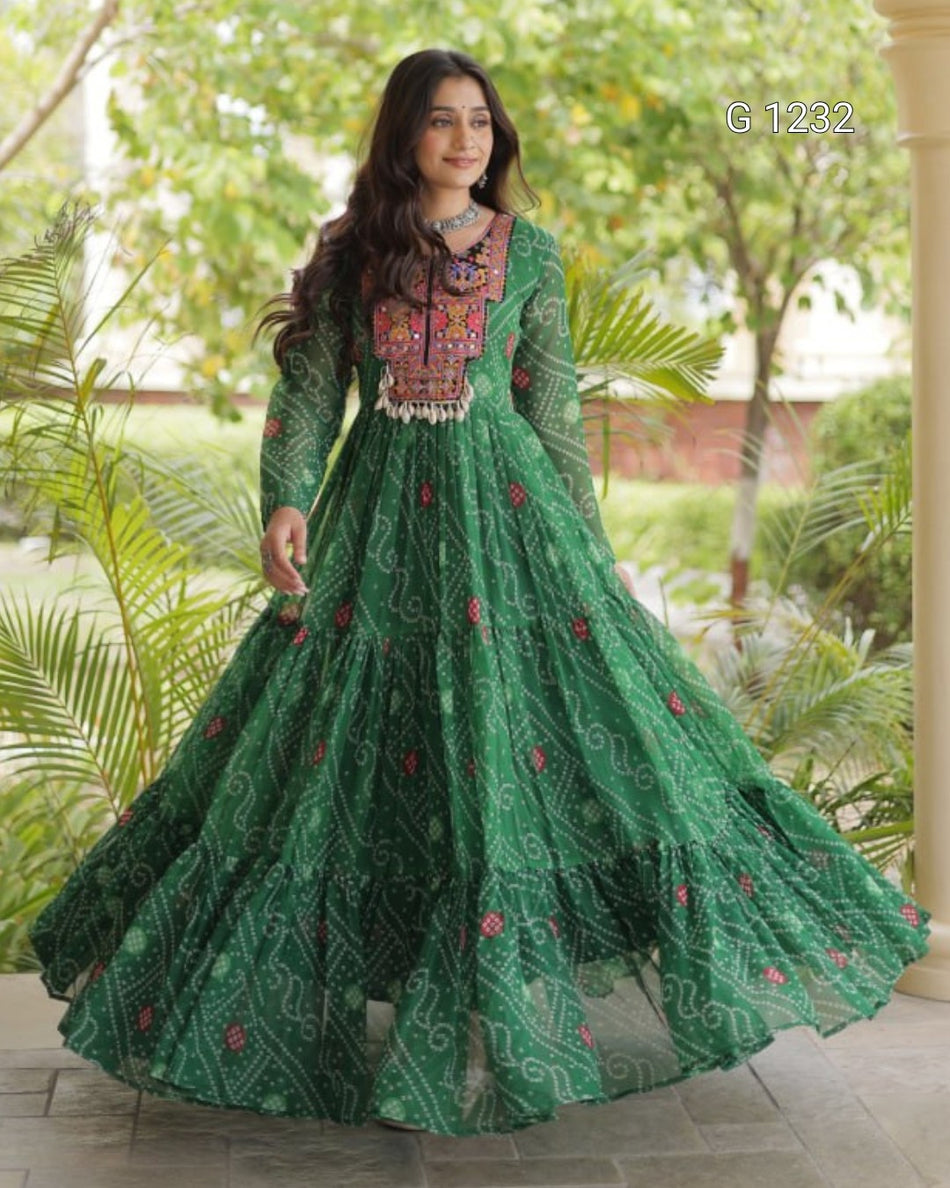 A woman wearing a green embroidered Anarkali gown with a heavily embellished neckline and a flared skirt, standing outdoors in front of green foliage.