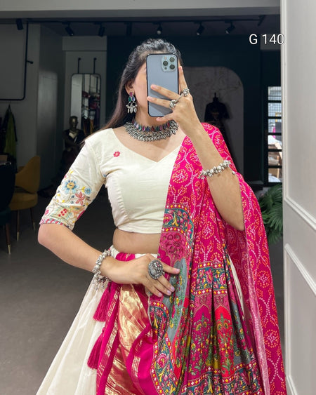 Woman in a white blouse and pink saree with intricate patterns, standing indoors.