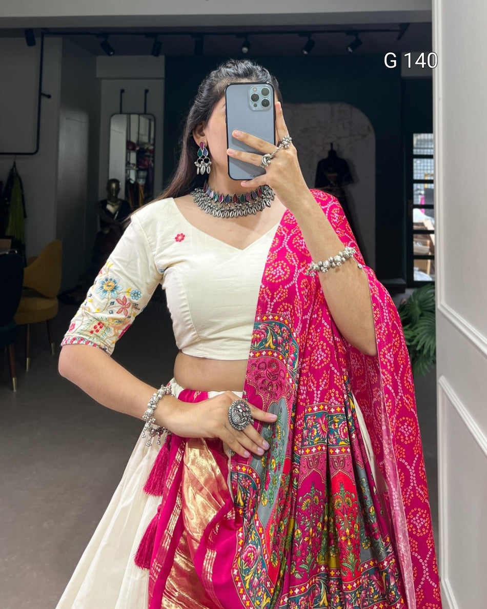 Woman in a white blouse and pink saree with intricate patterns, standing indoors.