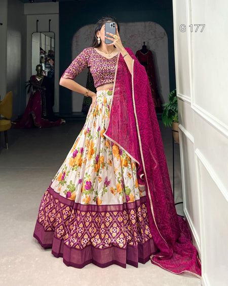 Woman wearing a colorful traditional outfit with a floral skirt and purple dupatta in a room.
