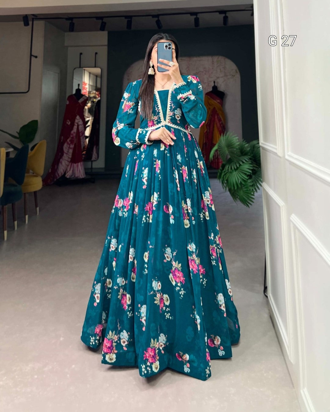 Woman wearing a teal floral dress in a room with white walls and a plant.