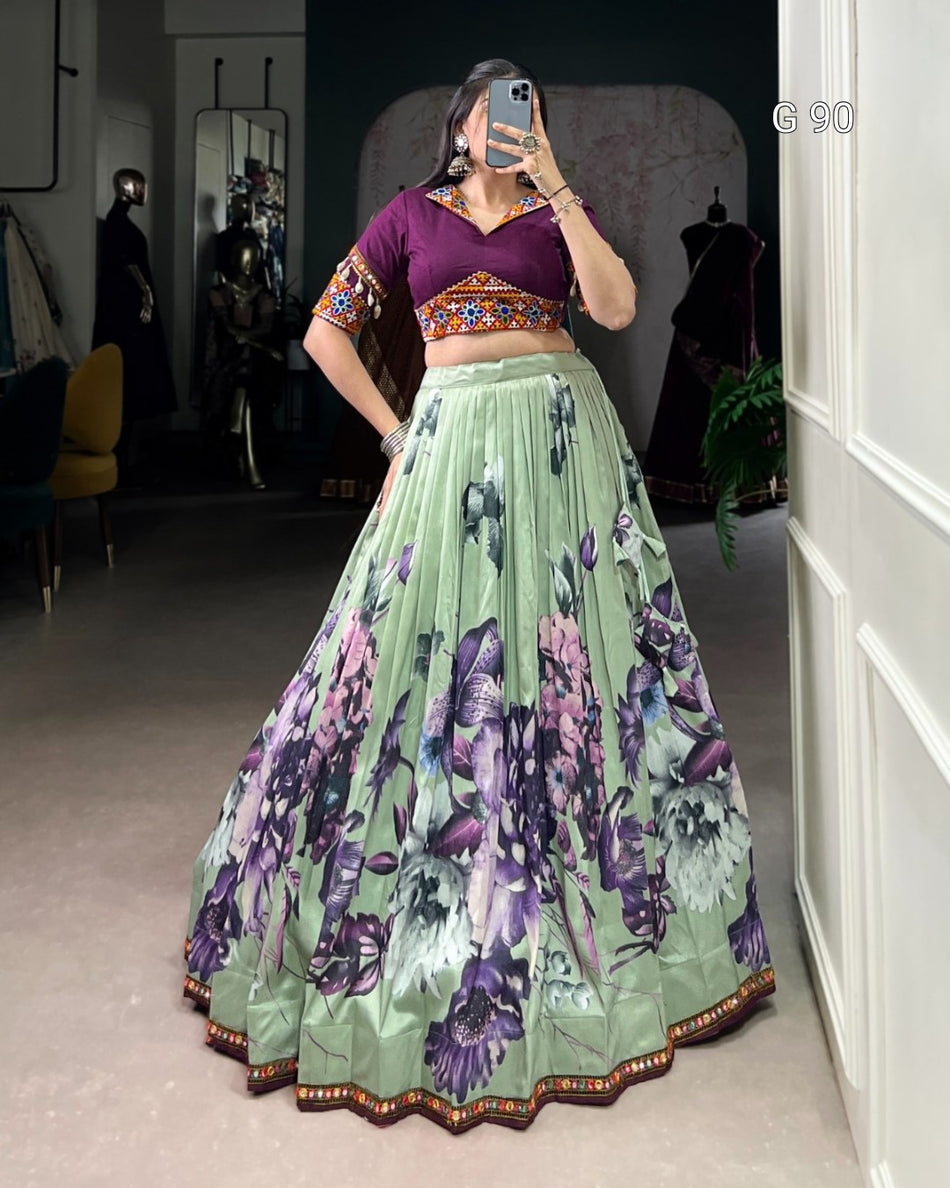 Person wearing a traditional outfit with a purple top and green floral skirt in a room.