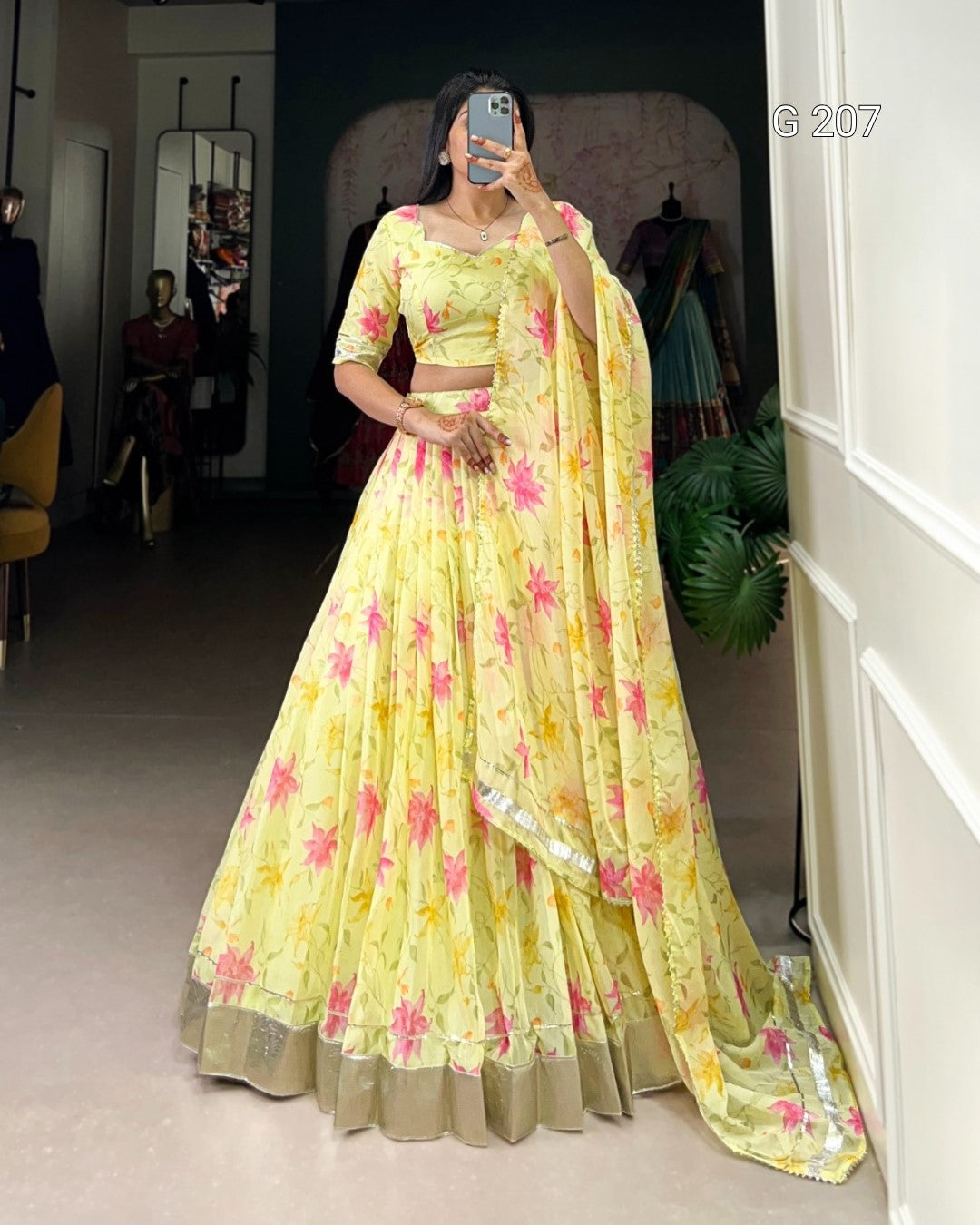 Woman wearing a yellow floral saree with a matching blouse in a room.