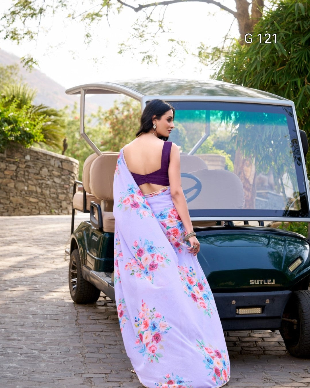 Woman in a floral saree standing next to a golf cart with a scenic background
