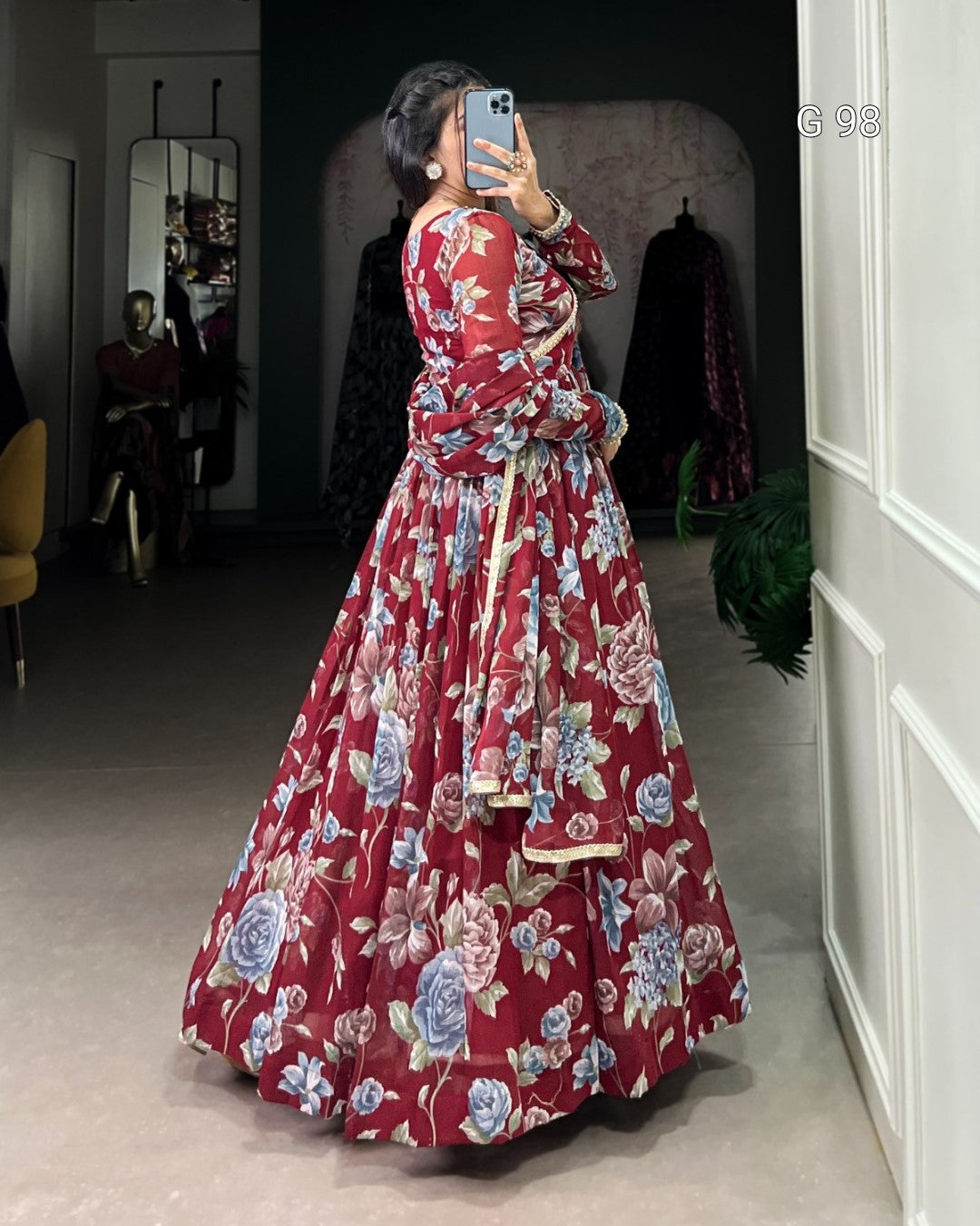 Person wearing a red floral dress taking a mirror selfie in a room.