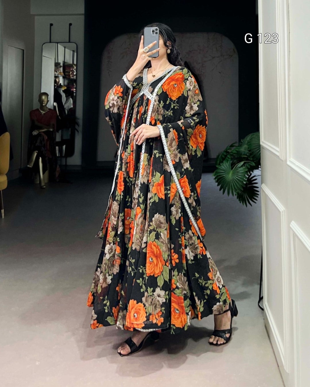 Woman taking a mirror selfie wearing a floral dress with orange flowers in a room.
