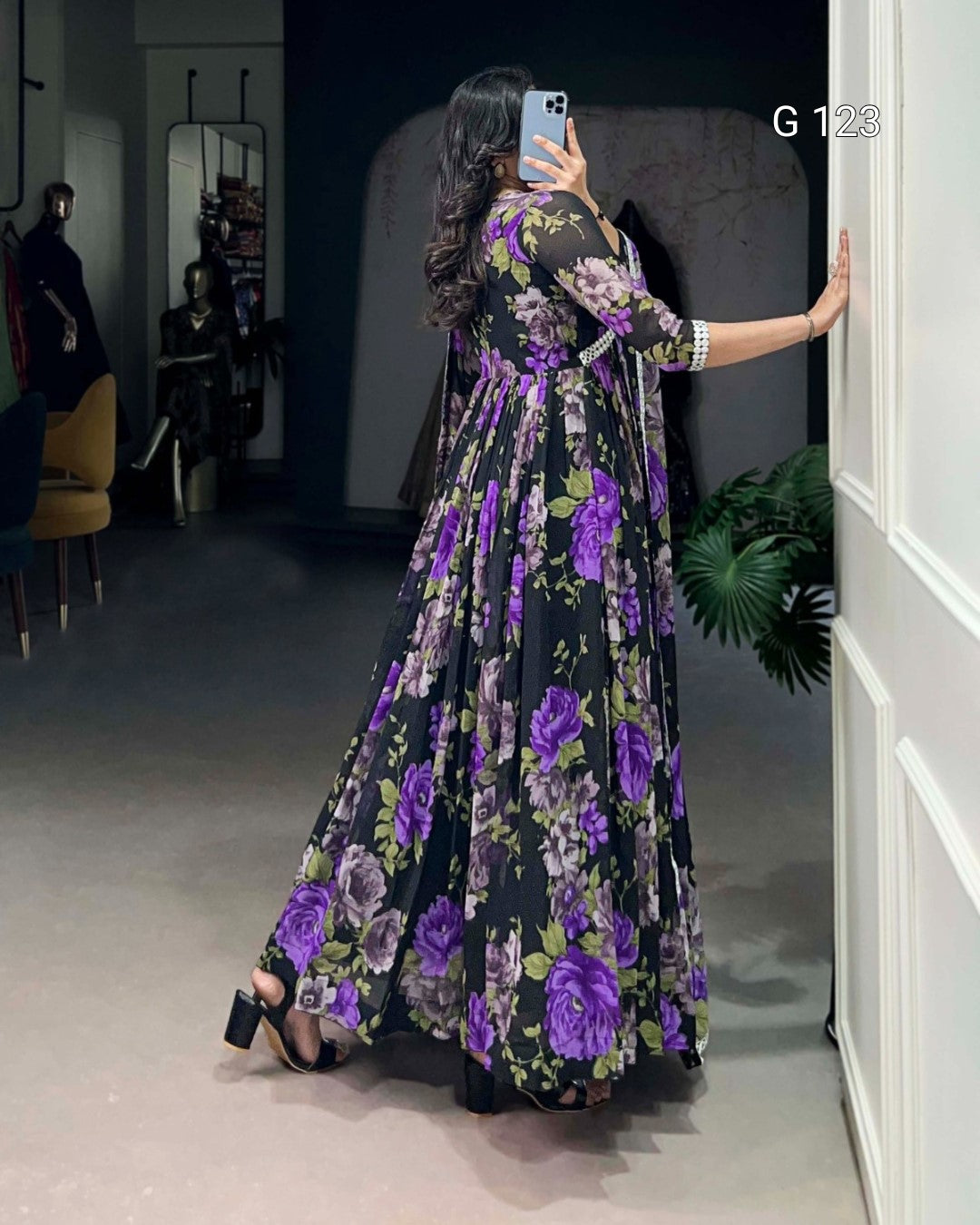 Woman in a floral dress taking a mirror selfie in a room.
