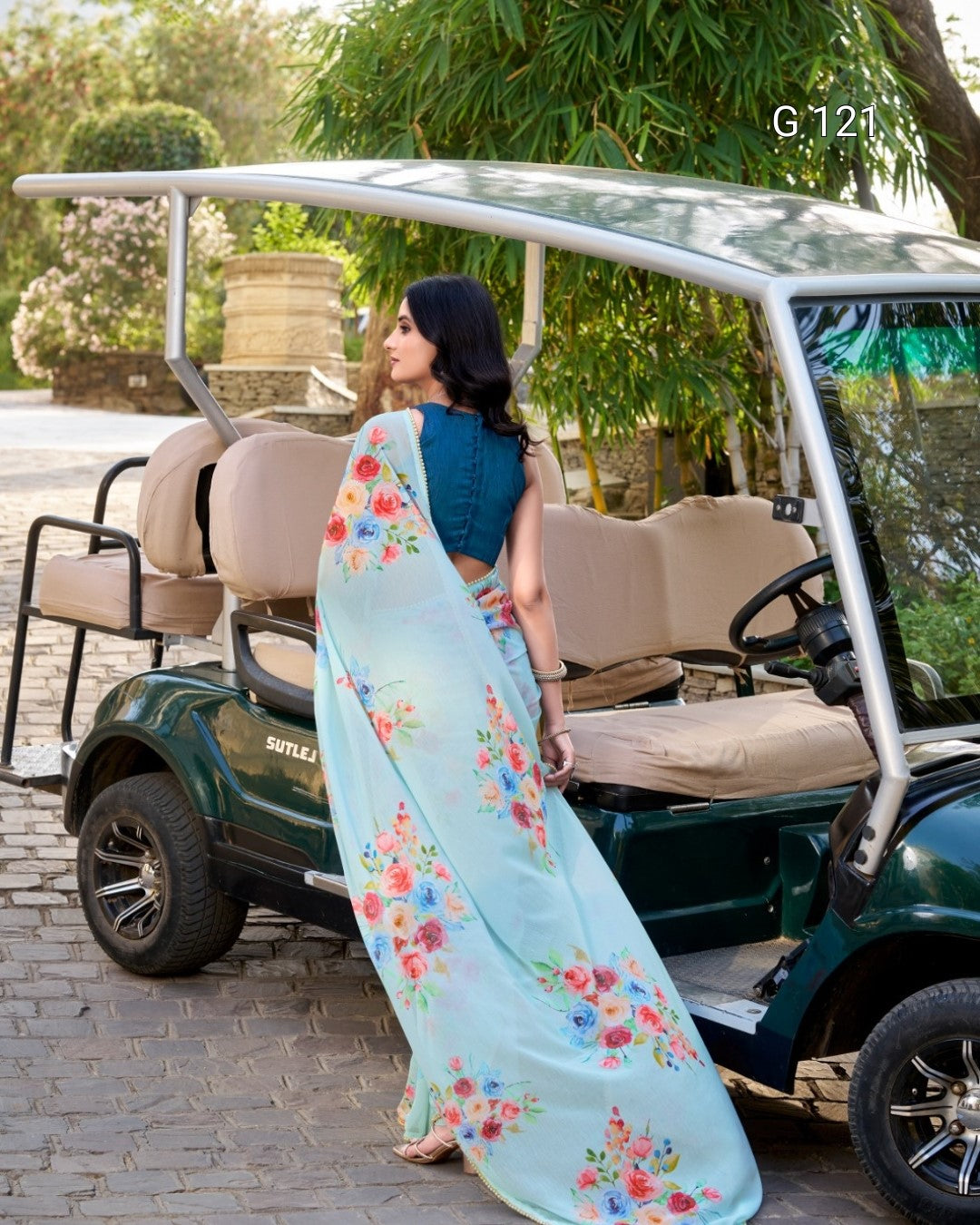 Woman in a floral saree standing next to a golf cart in a park-like setting