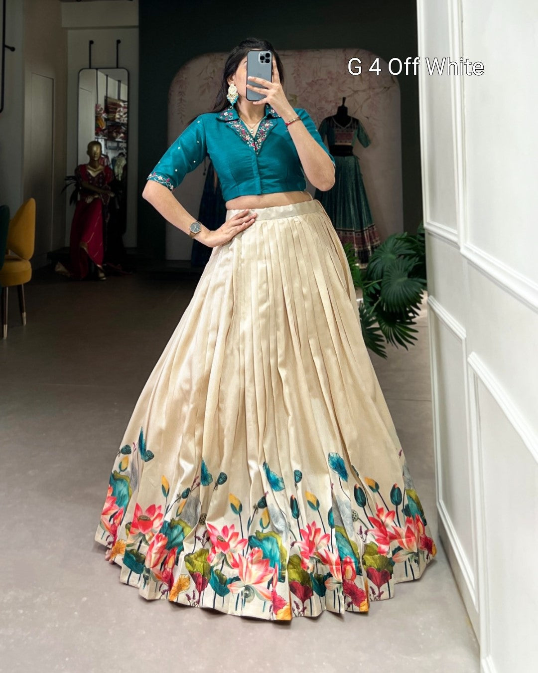Woman wearing a teal blouse and beige floral skirt in a room.