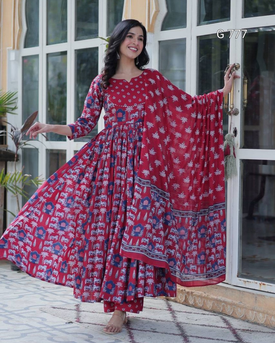 Woman wearing a red floral dress standing in front of a glass door.