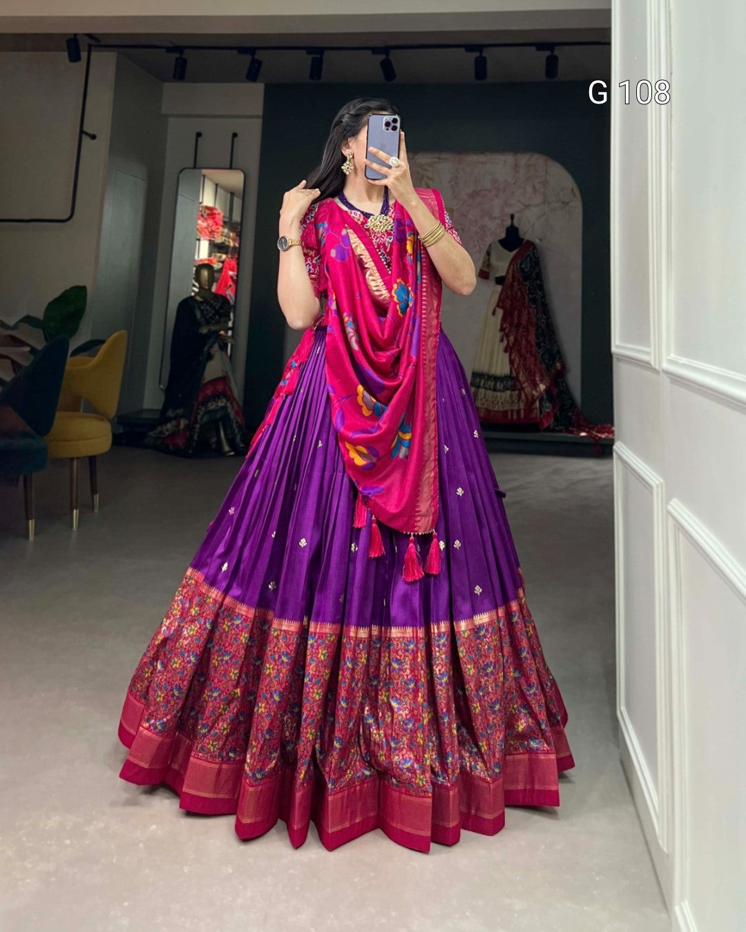 Person wearing a vibrant purple and pink traditional outfit with a colorful dupatta in a room.