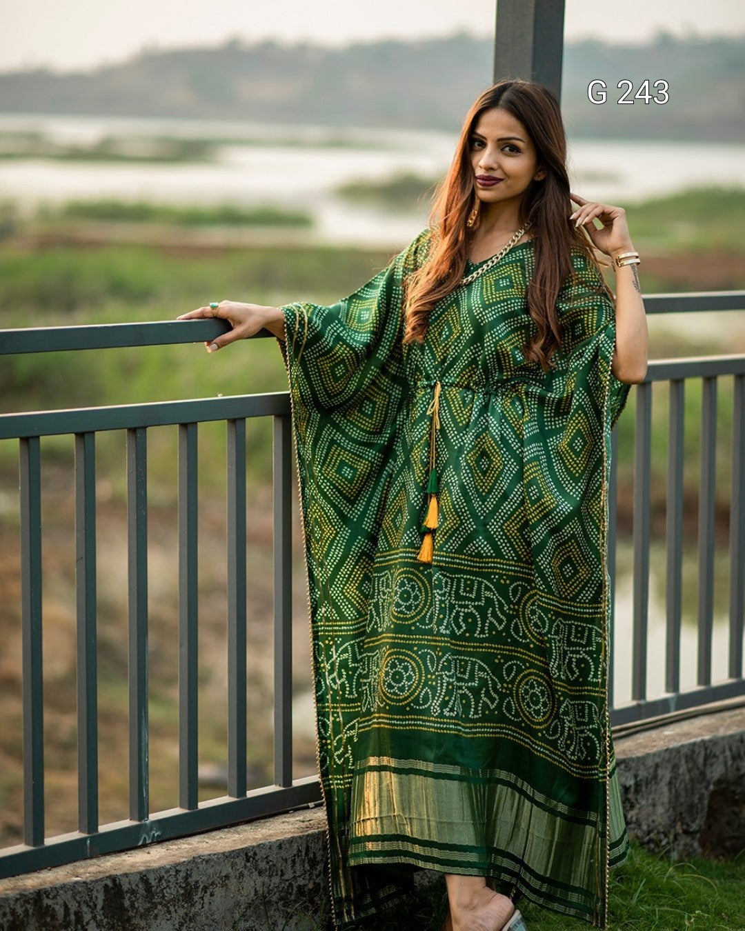 Woman wearing a green patterned dress standing on a balcony with a scenic background