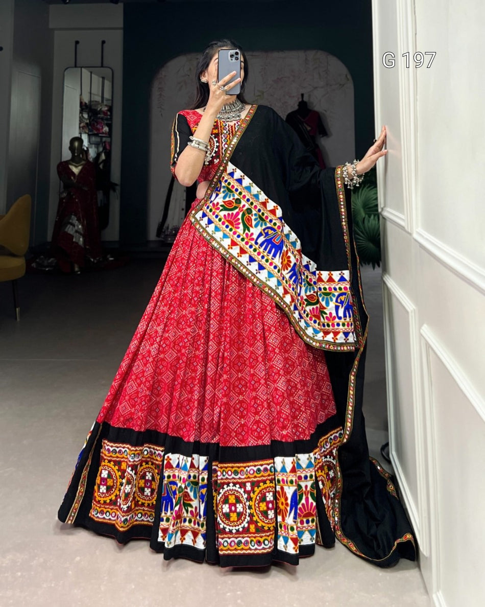 Person wearing a vibrant red and black traditional outfit with colorful patterns, standing in a room.