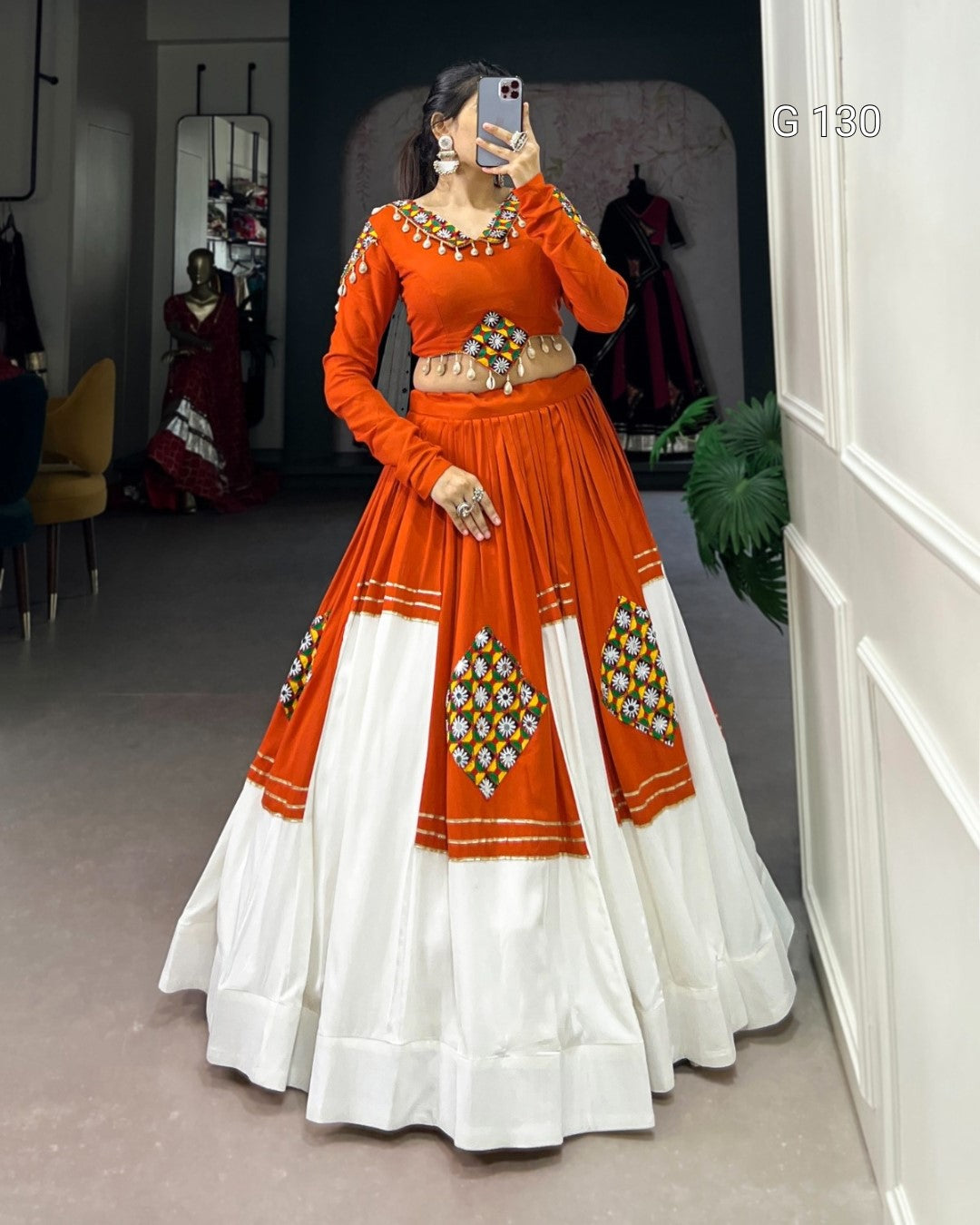 Person wearing an orange and white traditional outfit with intricate designs, standing in a room.
