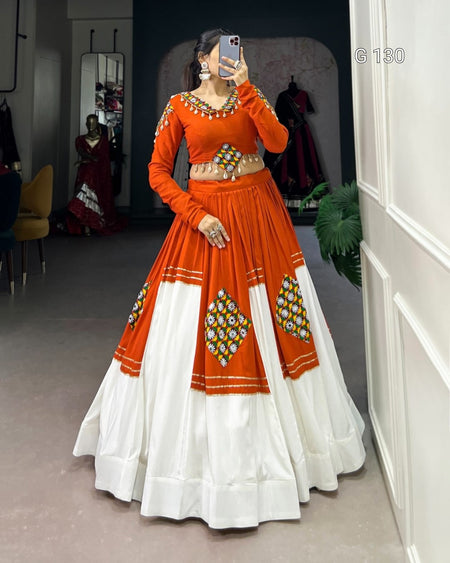 Person wearing an orange and white traditional outfit with intricate designs, standing in a room.