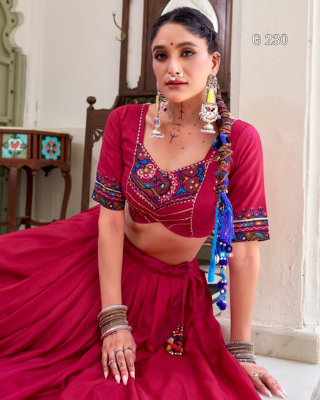 Woman in a traditional red outfit with colorful embellishments sitting indoors.
