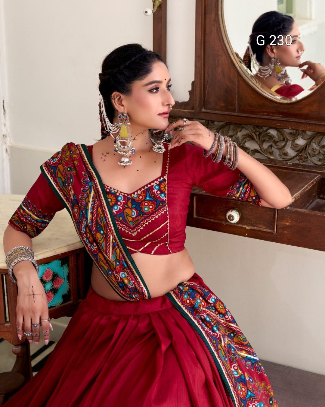 Woman in a traditional red saree with colorful embroidery, sitting in front of a mirror.