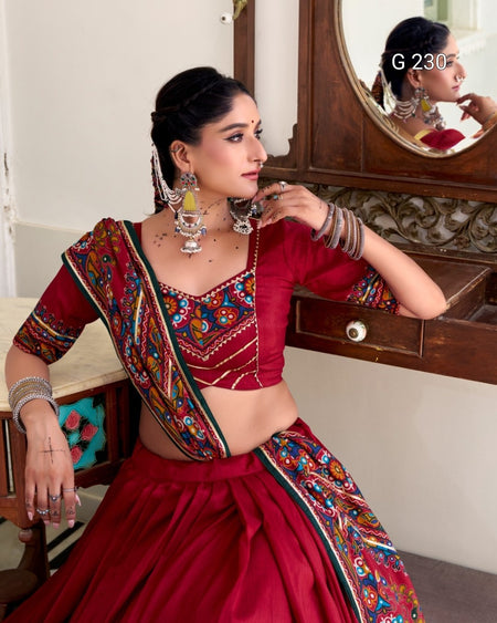 Woman in a traditional red saree with colorful embroidery, sitting in front of a mirror.