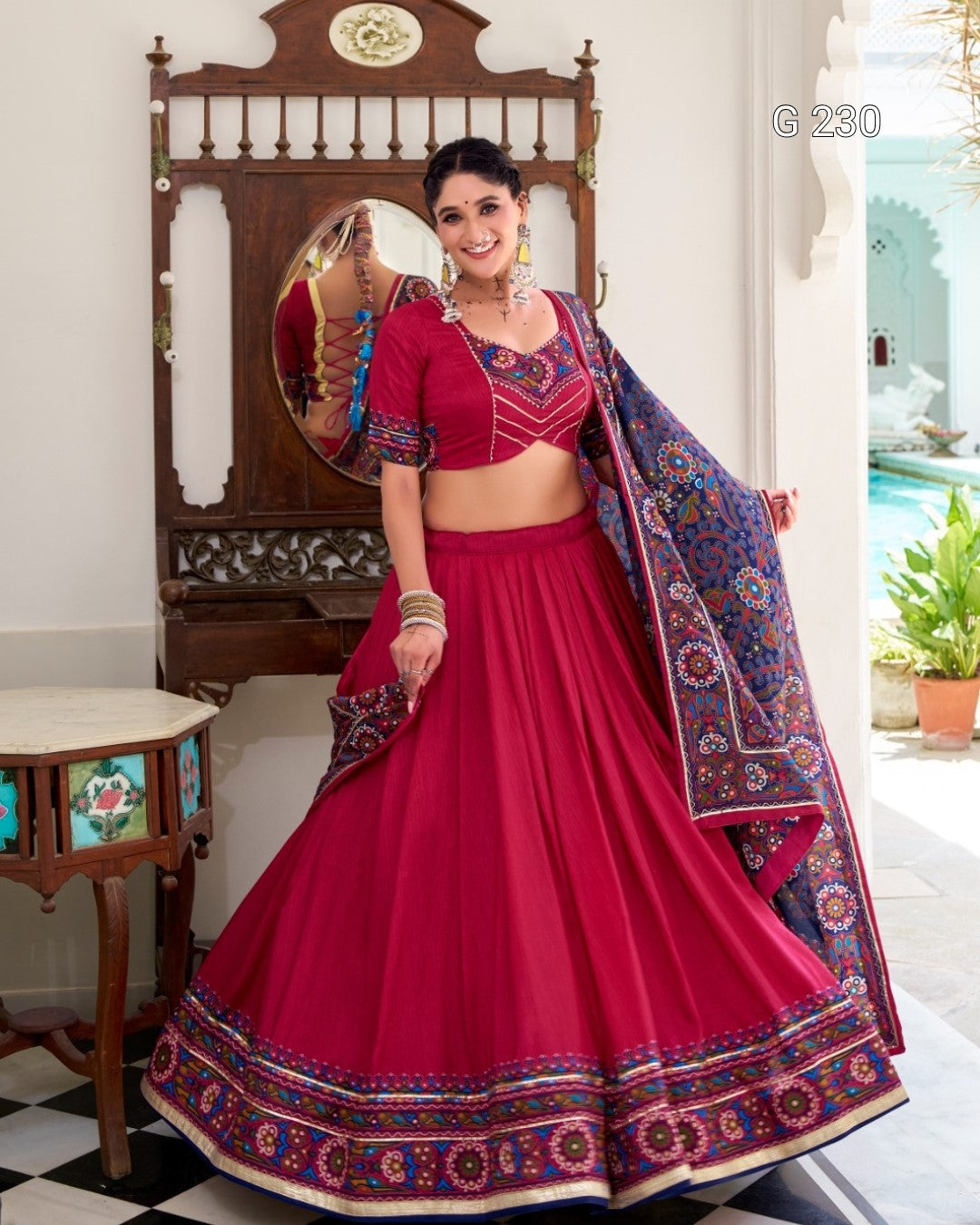 Woman in a red traditional outfit with a patterned dupatta in a decorated room.