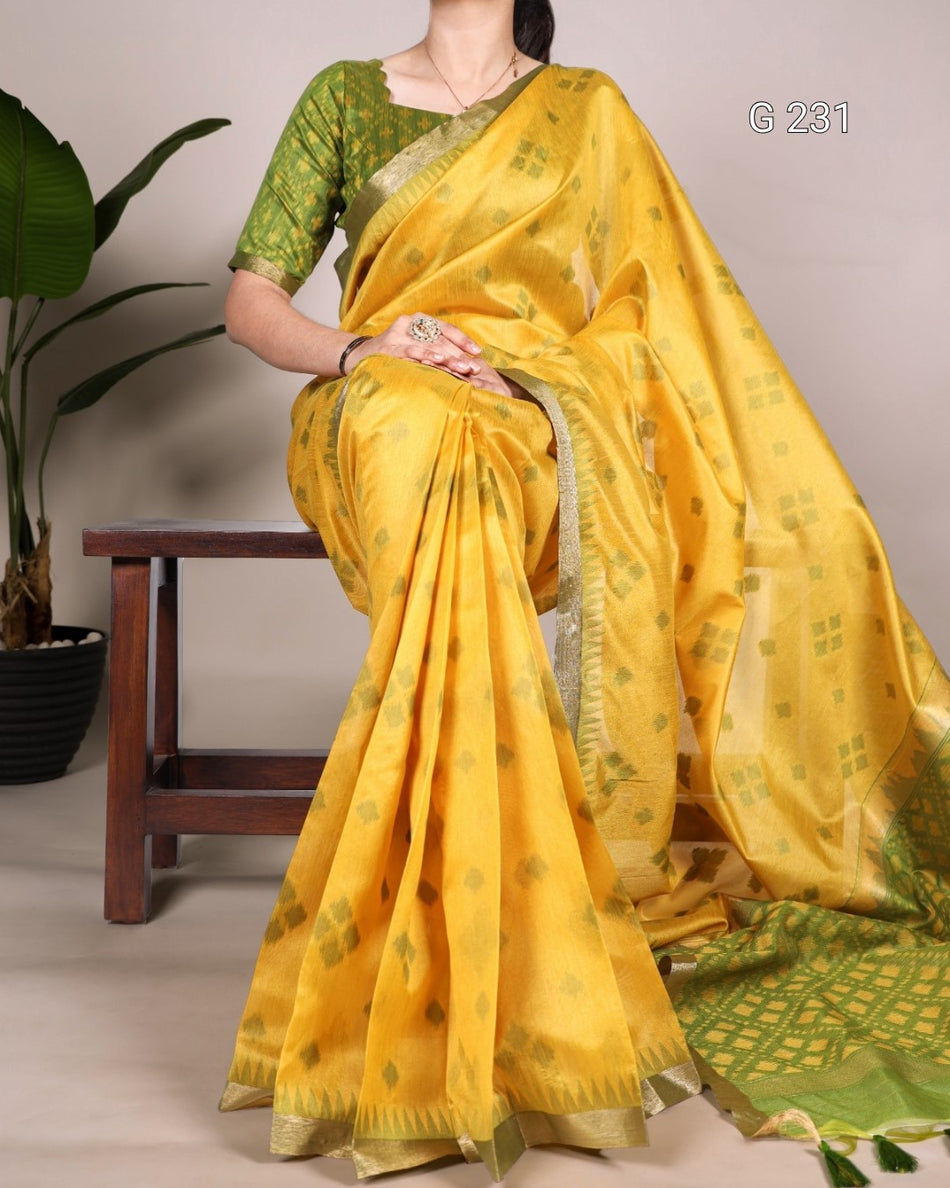 Woman wearing a yellow saree with green border sitting on a chair.