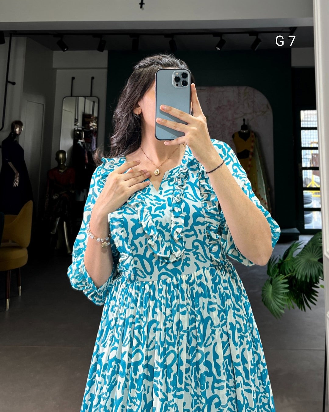 Person taking a mirror selfie wearing a blue patterned dress in an indoor setting.