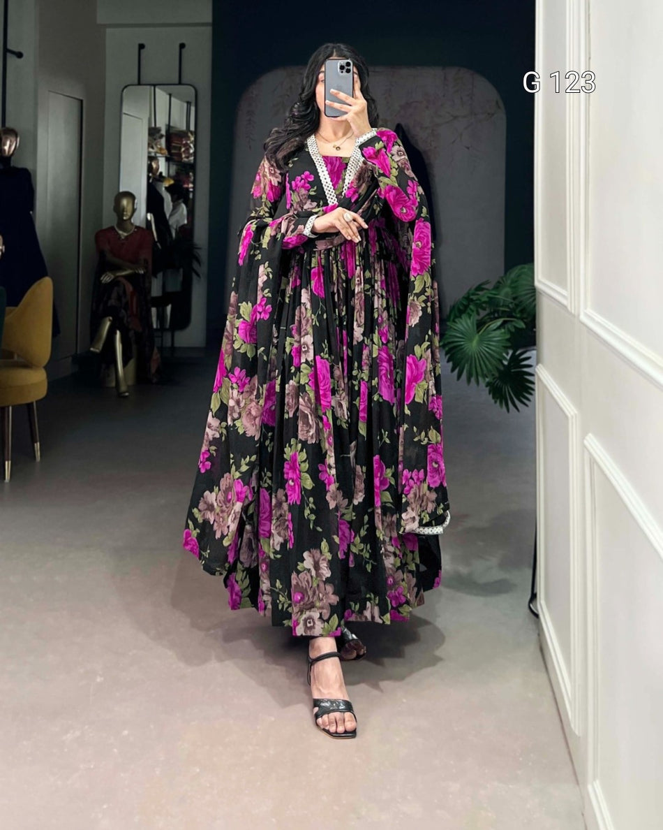 Woman wearing a long floral dress in a room with mirrors and a plant.
