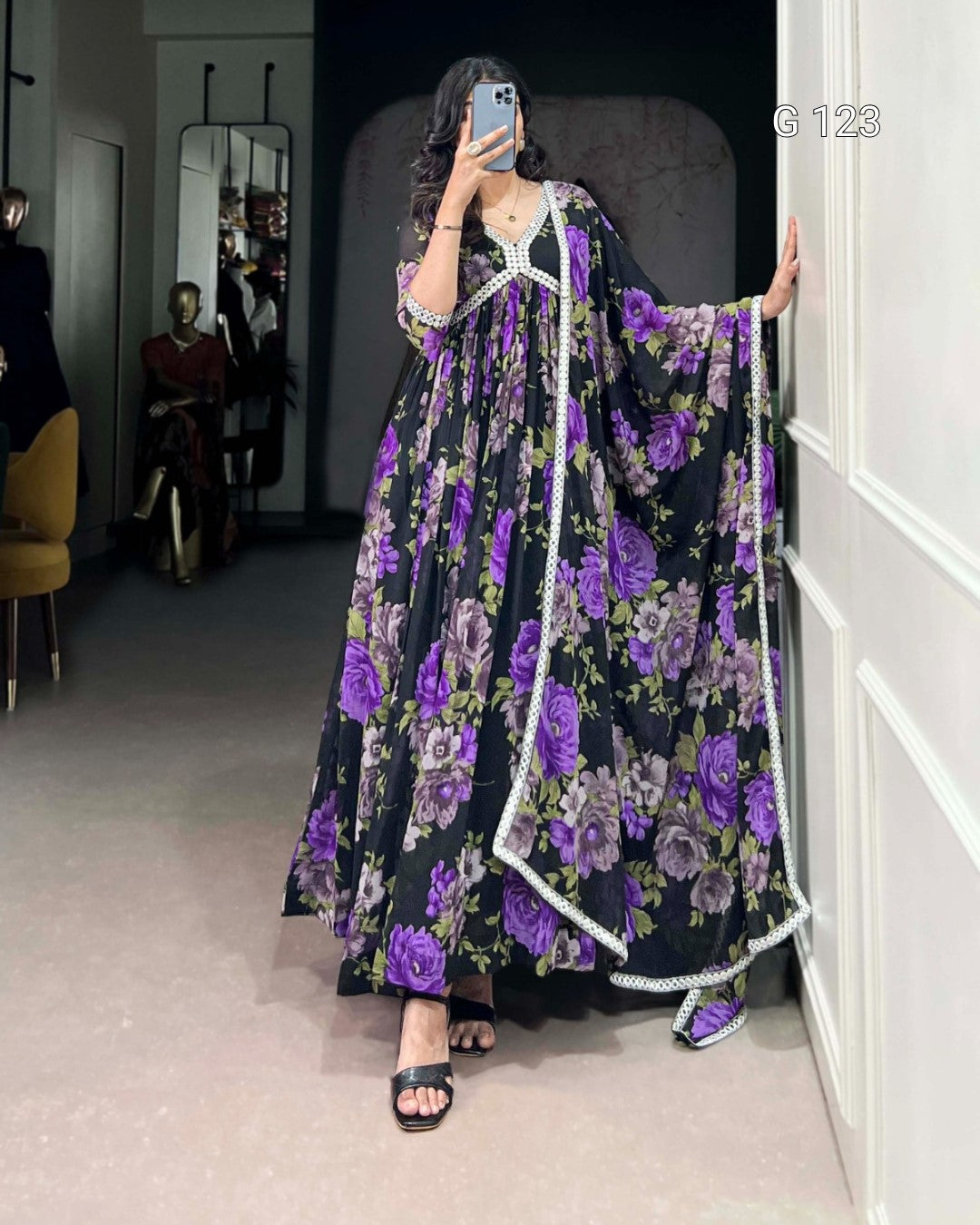 Person wearing a long, dark dress with purple floral patterns in a room.