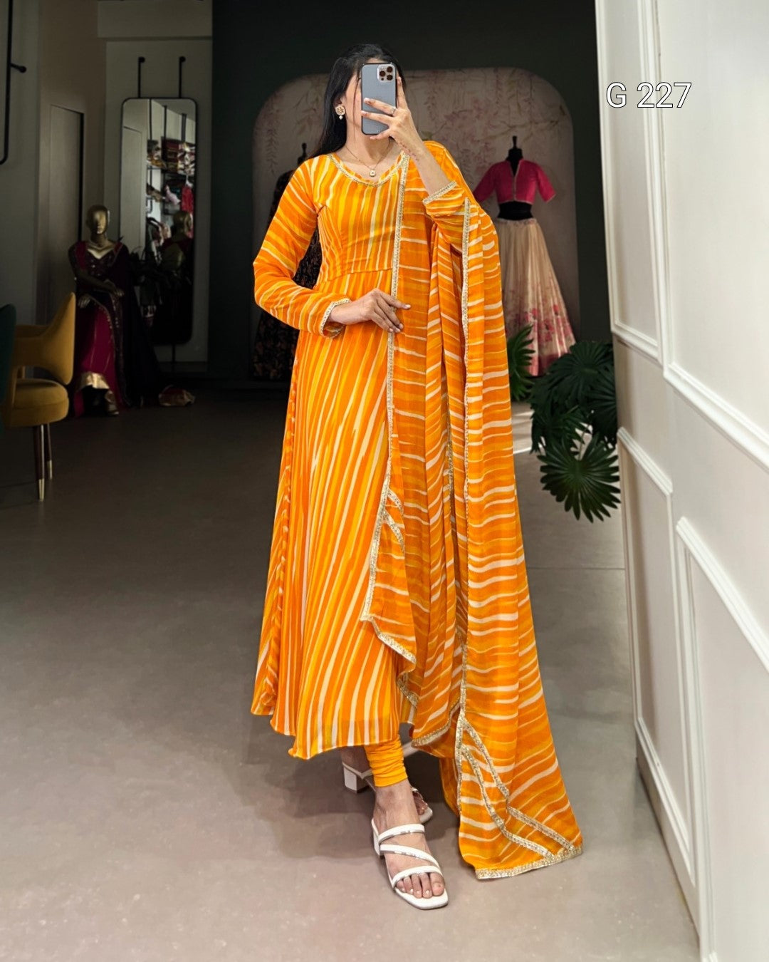 Woman taking a mirror selfie wearing an orange and yellow patterned dress in a room.