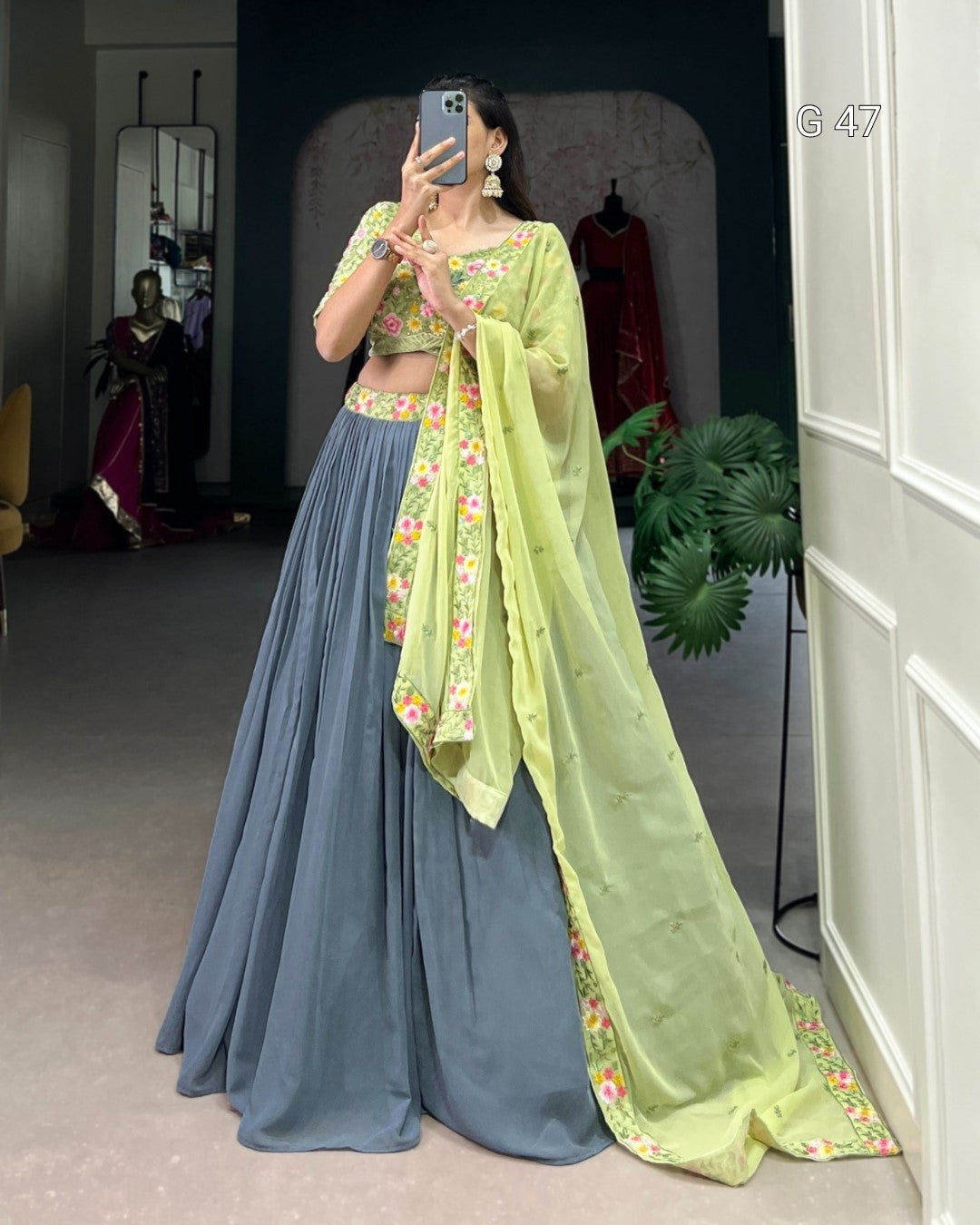 Person wearing a green and blue traditional outfit with a floral dupatta in a room.