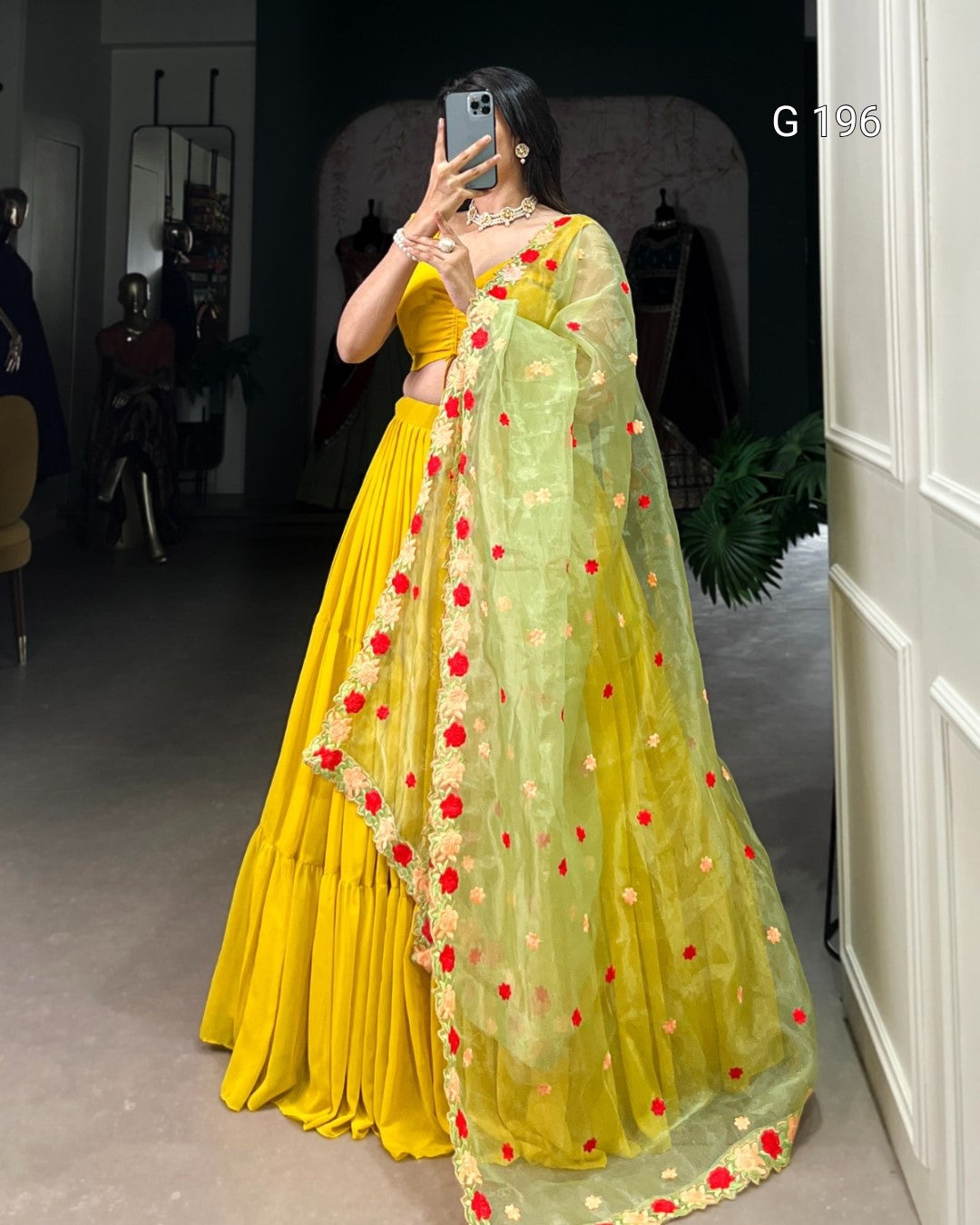Person wearing a yellow outfit with a green dupatta featuring red and orange patterns, standing in a room.