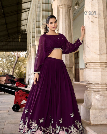 Woman in a purple traditional outfit standing in front of a stone building.