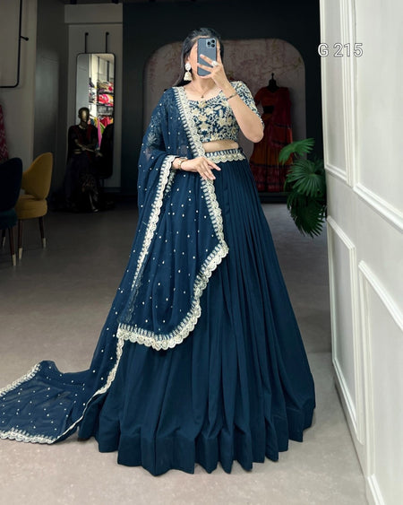 Woman wearing a traditional blue outfit with white embroidery in an indoor setting.