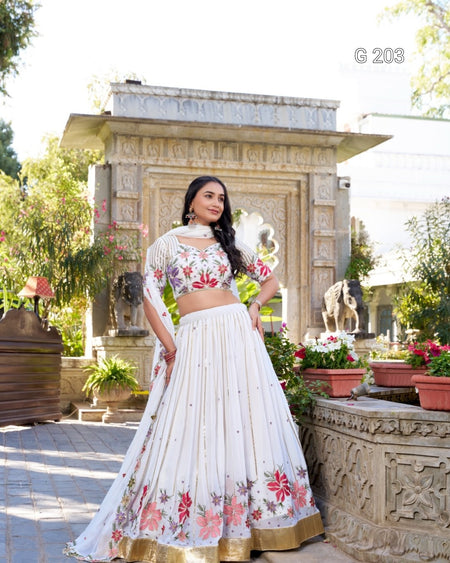 Woman in a white embroidered lehenga standing in front of a decorative stone structure with plants.