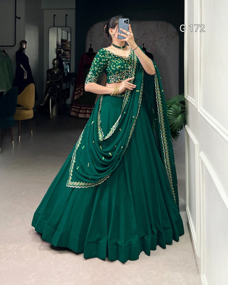 Woman in a green saree with gold details taking a mirror selfie.