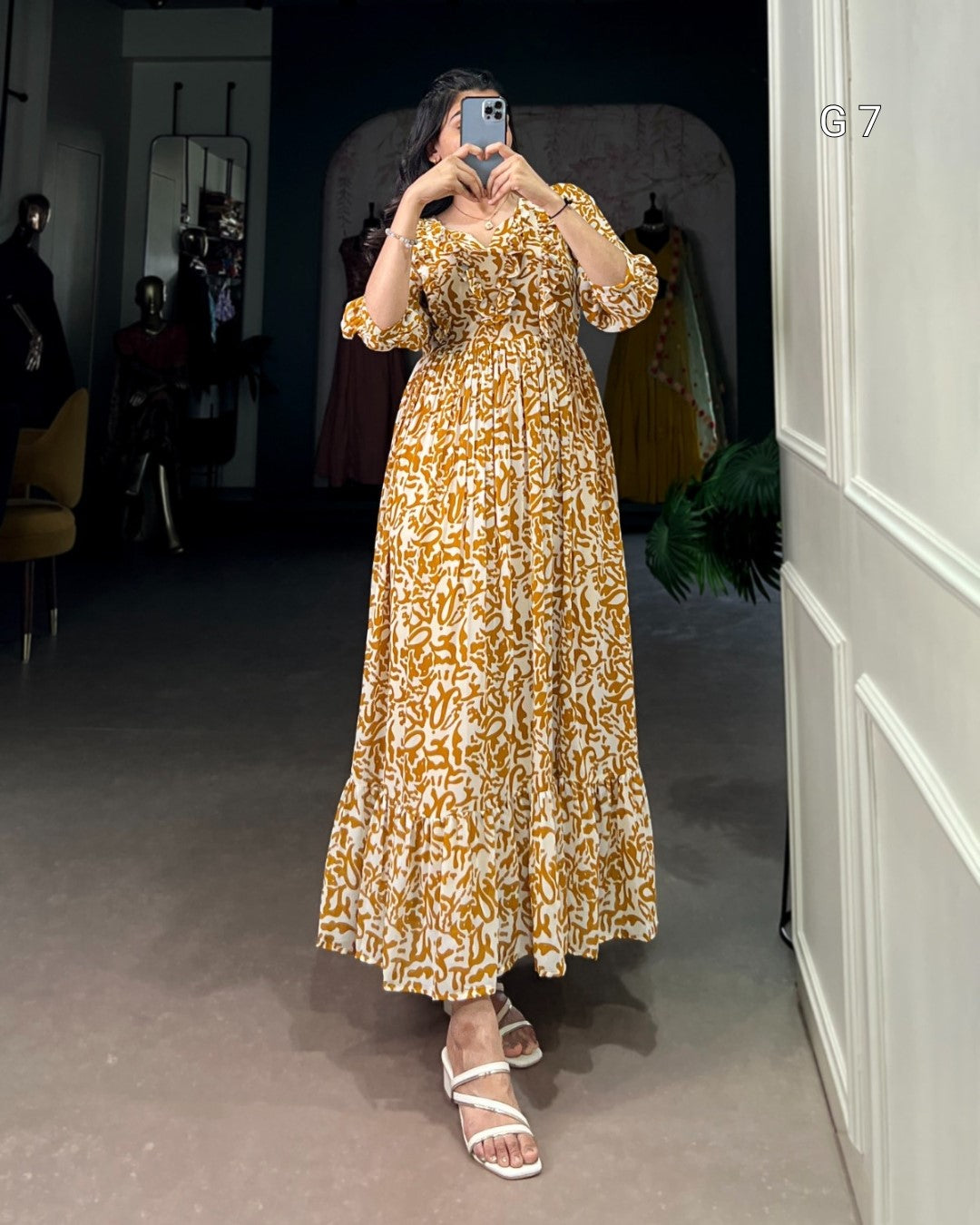 Woman taking a mirror selfie wearing a gold and white patterned dress in a room.
