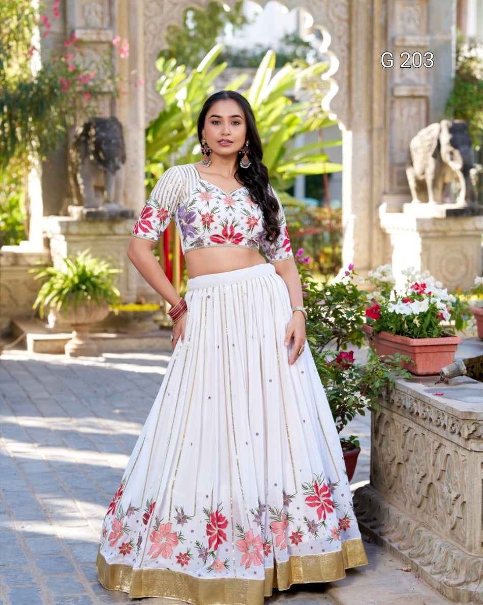 Woman wearing a floral embroidered outfit in an outdoor setting with plants and statues.