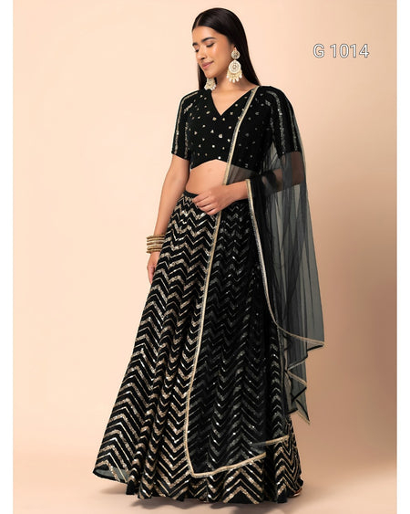 A woman modeling a black and silver chevron-patterned lehenga choli with a sheer black dupatta, set against a solid beige studio background.