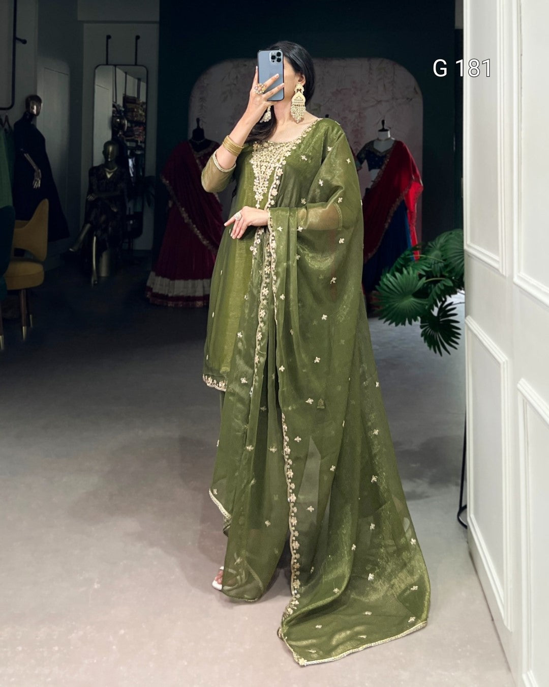 Person wearing a green traditional outfit with intricate designs in a room setting.