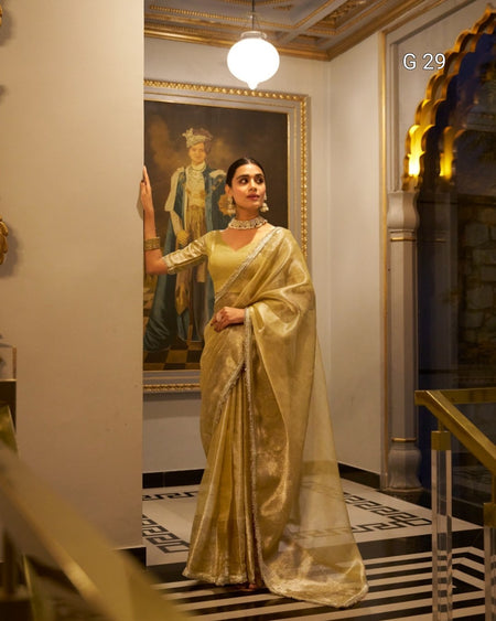 Woman in a gold saree standing in an ornate room with a painting on the wall.