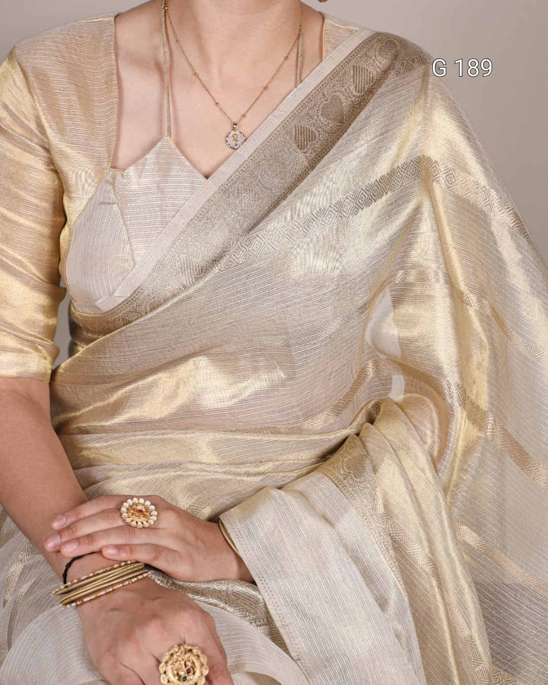 Gold saree with intricate patterns and jewelry on a neutral background
