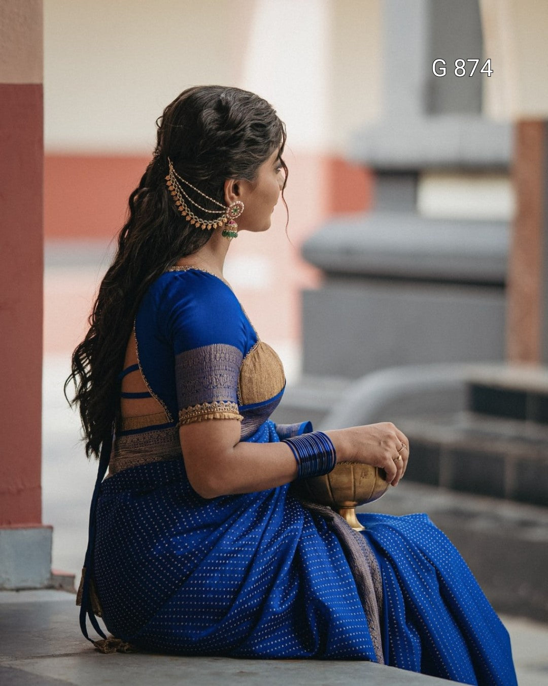 Woman in a blue saree sitting outdoors with architectural elements in the background