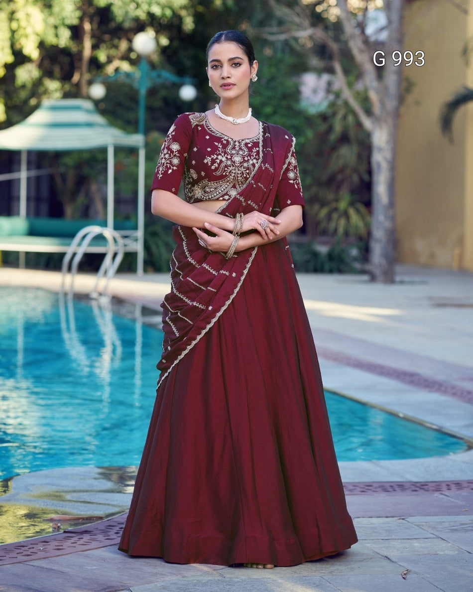 A woman stands outdoors by a swimming pool wearing a long maroon lehenga choli with gold embroidery. The image includes the text 'G 993' in the upper right corner.