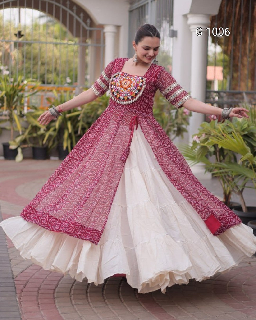 A woman wearing a traditional Indian salwar suit with a pink printed kurta and a cream-colored flared skirt, captured in a courtyard setting. The text 'G 1006' is visible in the top right corner.